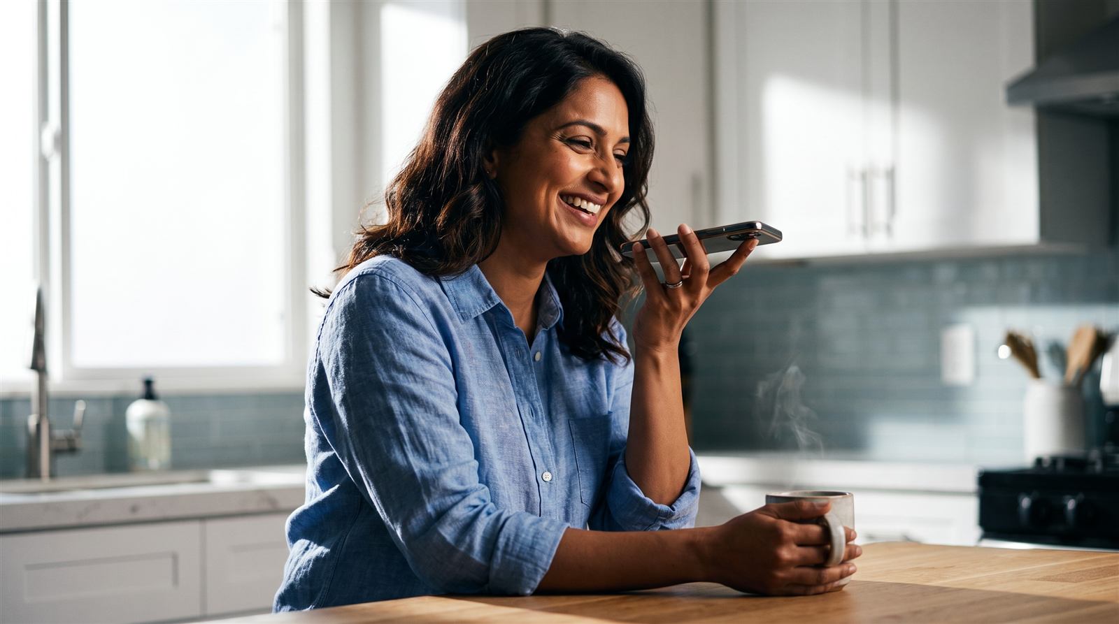 A younger woman on a sofa, speaking into her phone as she records a voice note.